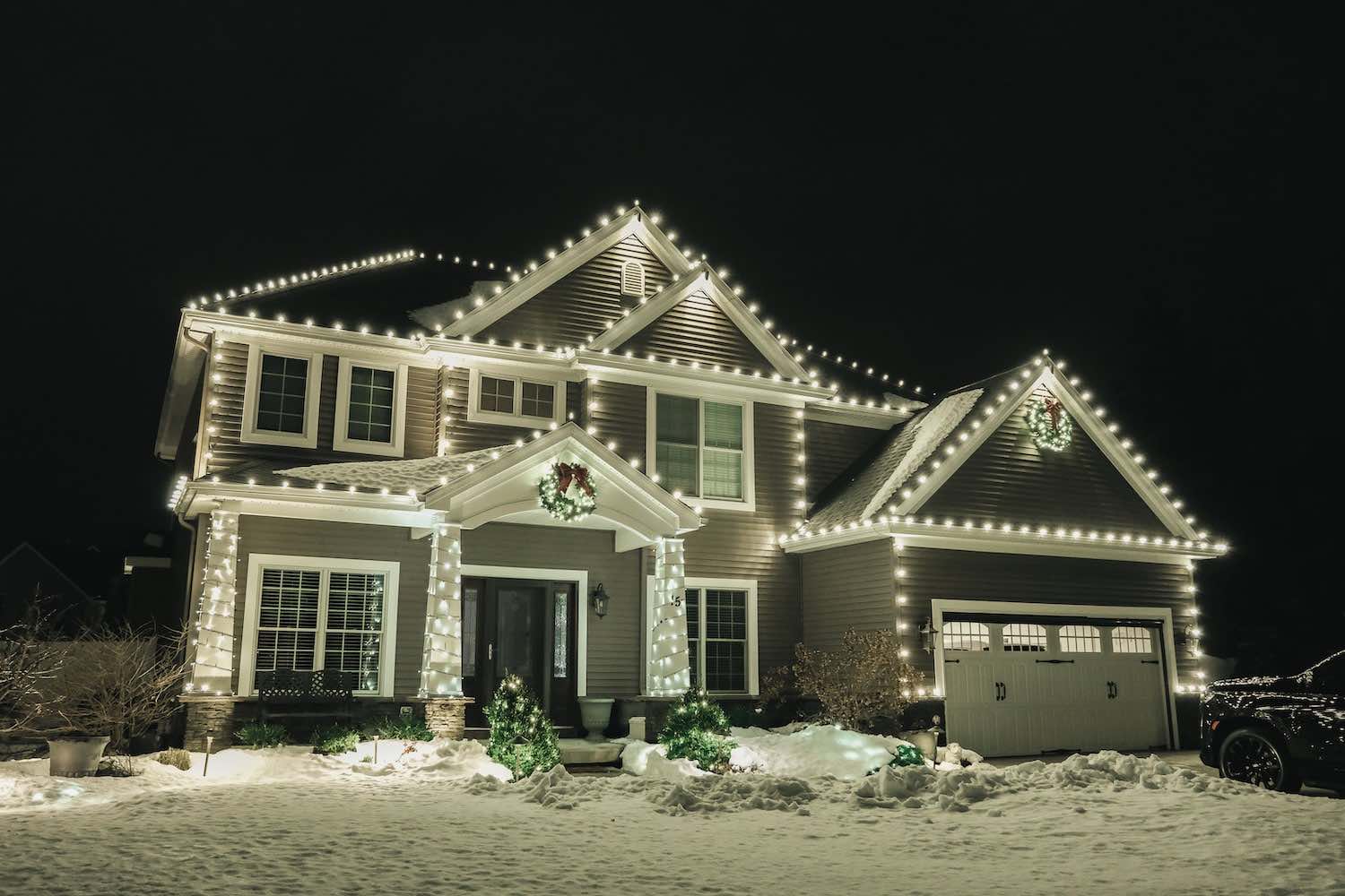 Two-story home with white Christmas lights on the rooflines after a snowfall