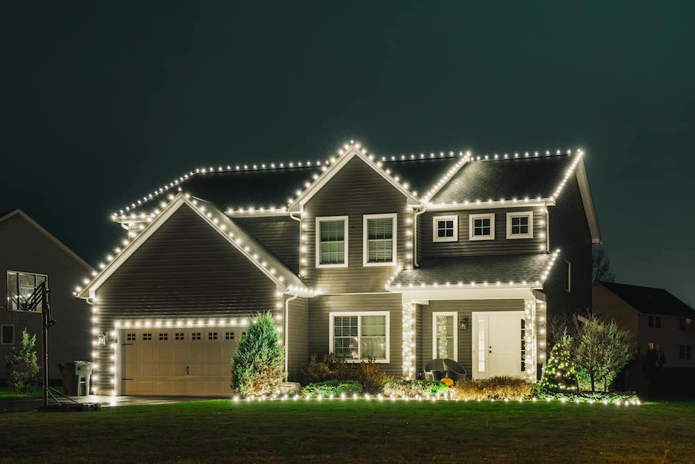 Two-story gray house outlined in warm white Christmas lights at night