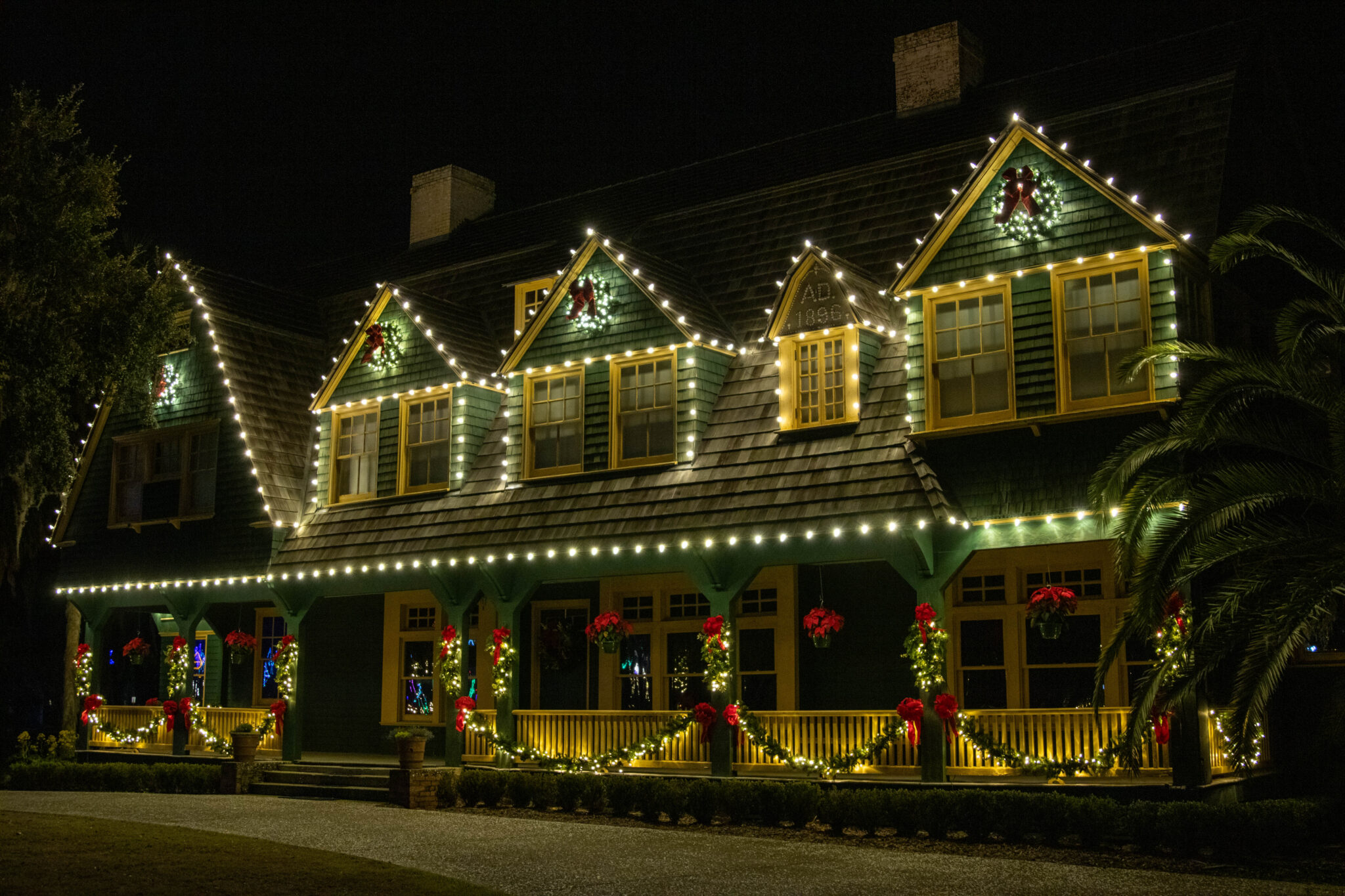 Two-story home with warm white Christmas lights along the rooflines and porch at night